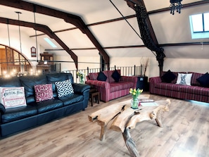 A spacious loft with exposed wooden beams, a black leather sofa, a striped red sofa, and a wooden coffee table. - Kaber Chapel (Kirkby Stephen)