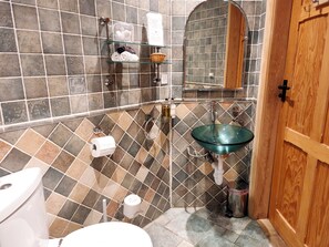 A bathroom with a glass sink, a toilet, a shower area, and a wooden door. - Kaber Chapel (Kirkby Stephen)