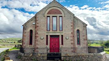 Un edificio de piedra con puerta roja, ventanas arqueadas y camino de entrada de grava.