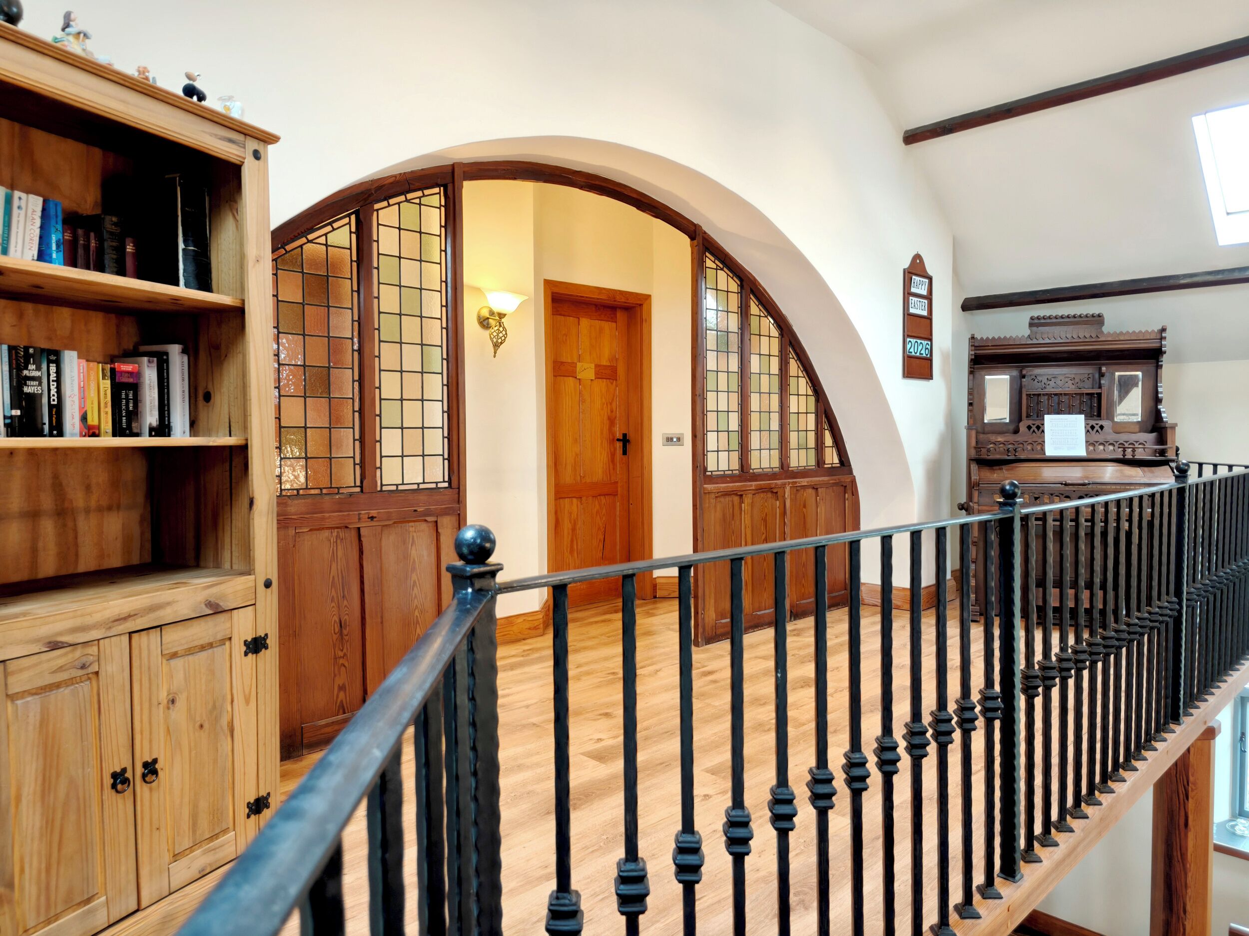 Eine Holztreppe mit schwarzer Geländer, ein Bücherregal mit Büchern und eine Tür mit dem Schild 'EASTER 2026'.