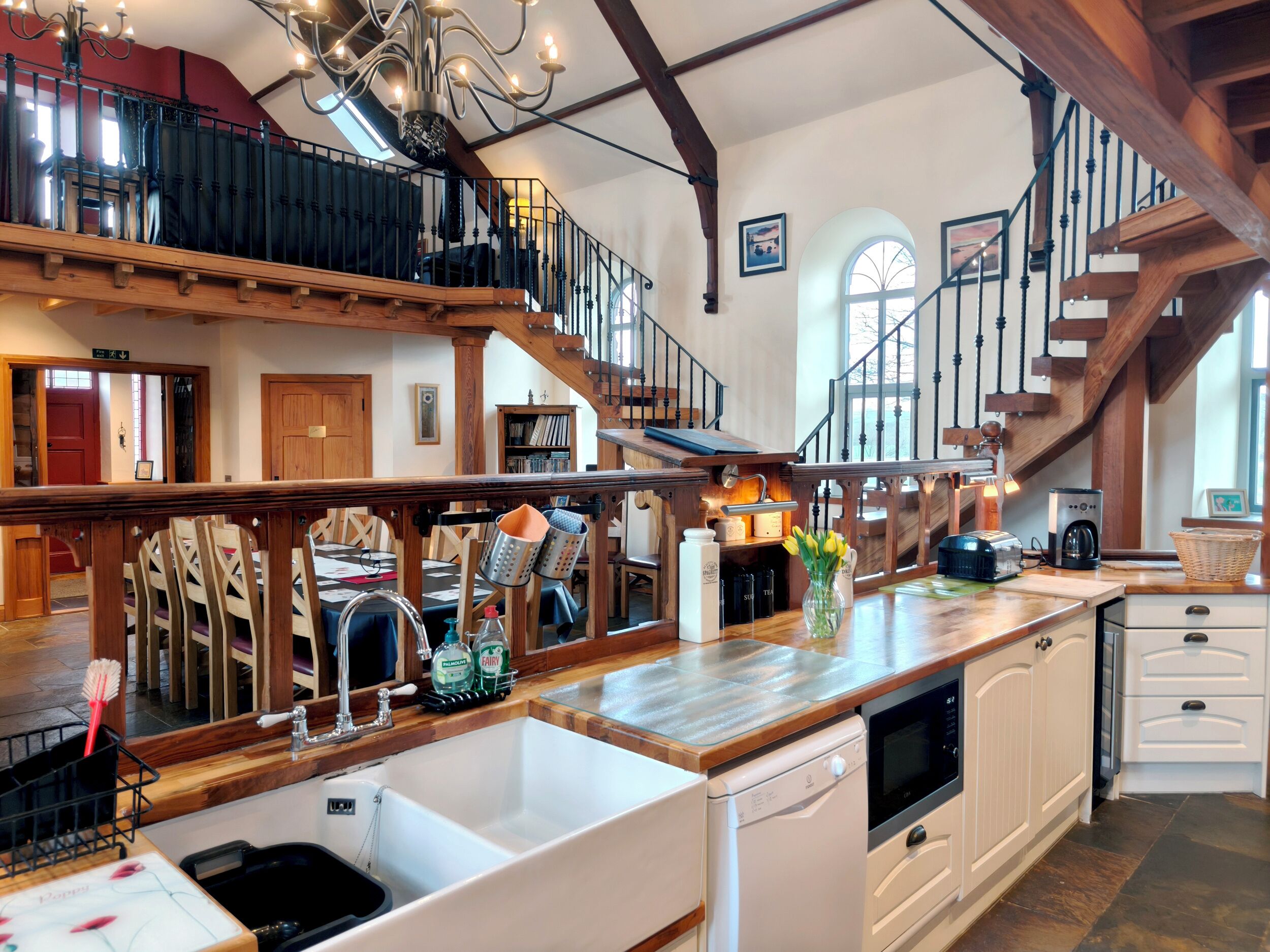 A spacious kitchen with a large island, wooden beams, a staircase, and a view of the upper floor.
