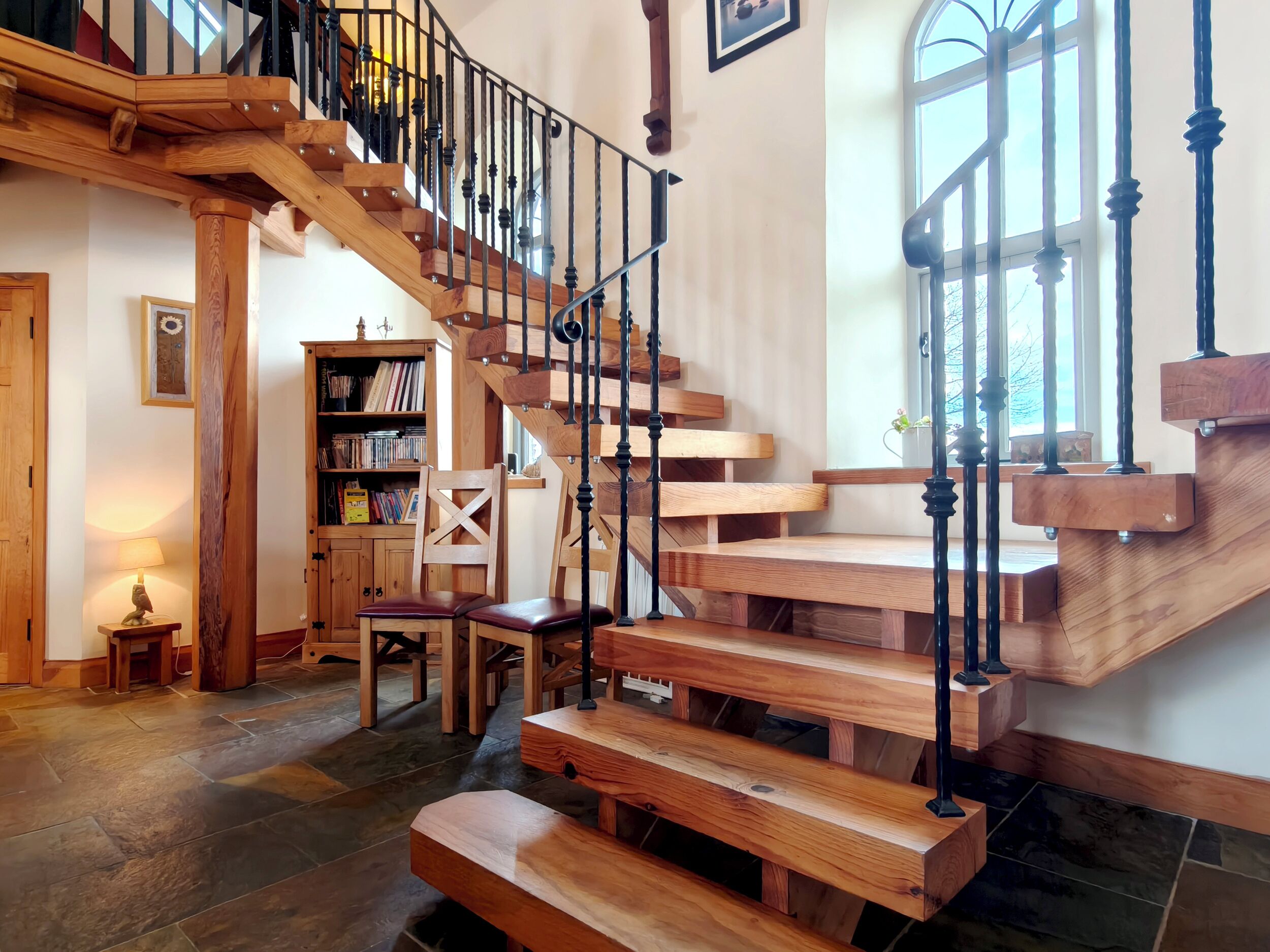 A wooden staircase with black railings, a wooden chair, a bookshelf, and a lamp.