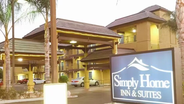 Entrada de hotel con un letrero que dice 'Simply Home Inn & Suites', una zona de estacionamiento techada y un edificio de varios pisos.