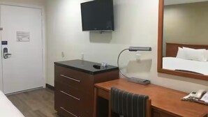 Habitación de hotel con una cama, un escritorio con lámpara, un televisor en la pared y una puerta.