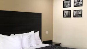 Una cama con almohadas blancas y un cabecero negro, una mesita de noche y cuatro fotografías blanco y negro en la pared.