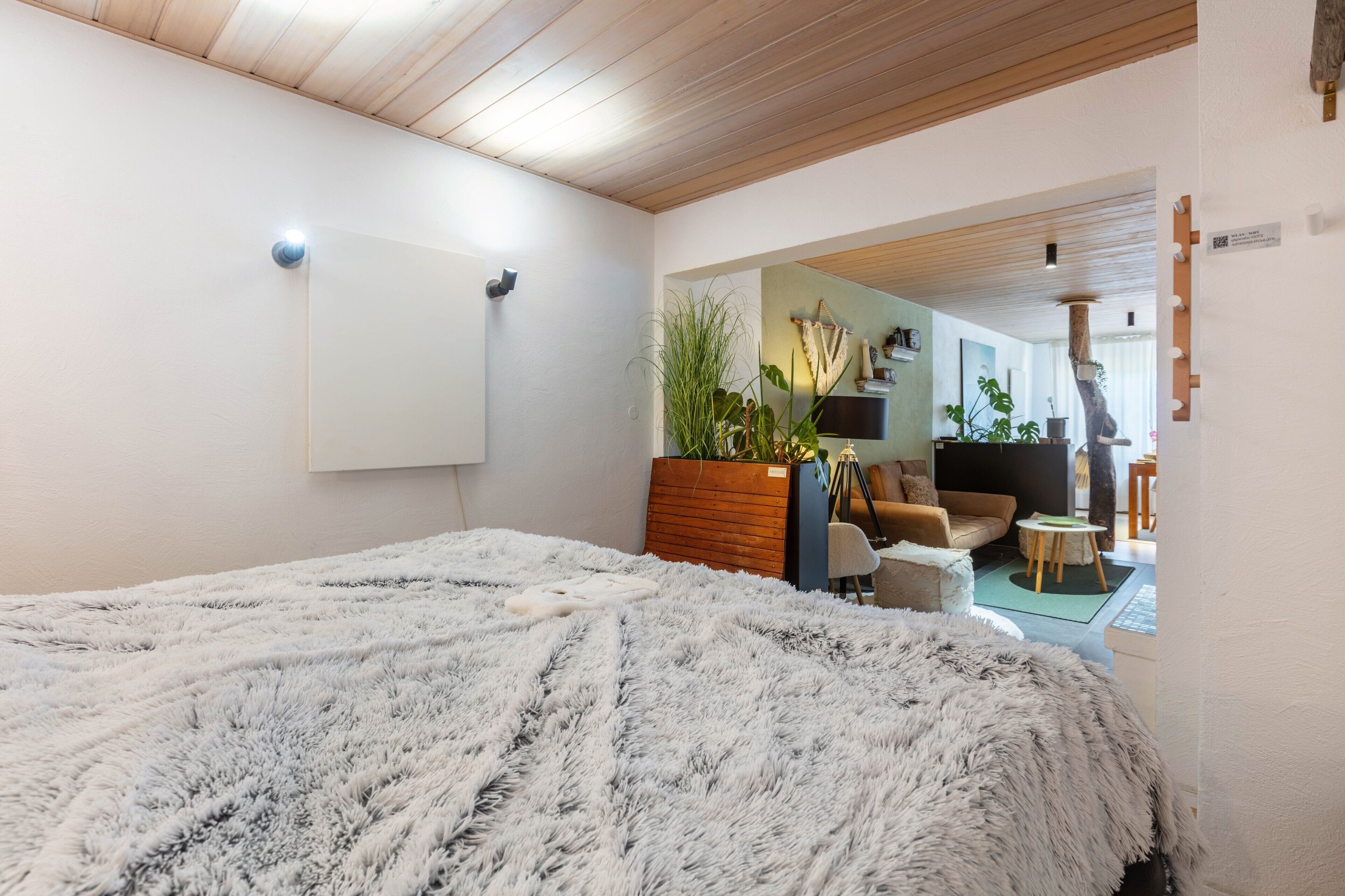Une chambre avec un grand lit, un plafond en bois, un tableau blanc, une plante, un canapé et une petite table.