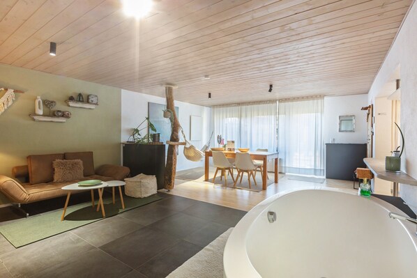 A modern living room with a sofa, coffee table, and a dining area with chairs and a table.