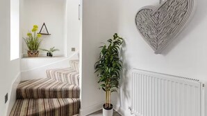 Un escalier recouvert d’une moquette à rayures, une plante en pot, un décor mural en forme de cœur et un radiateur.