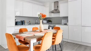 Une cuisine moderne avec des meubles blancs, un îlot central et des chaises orange.
