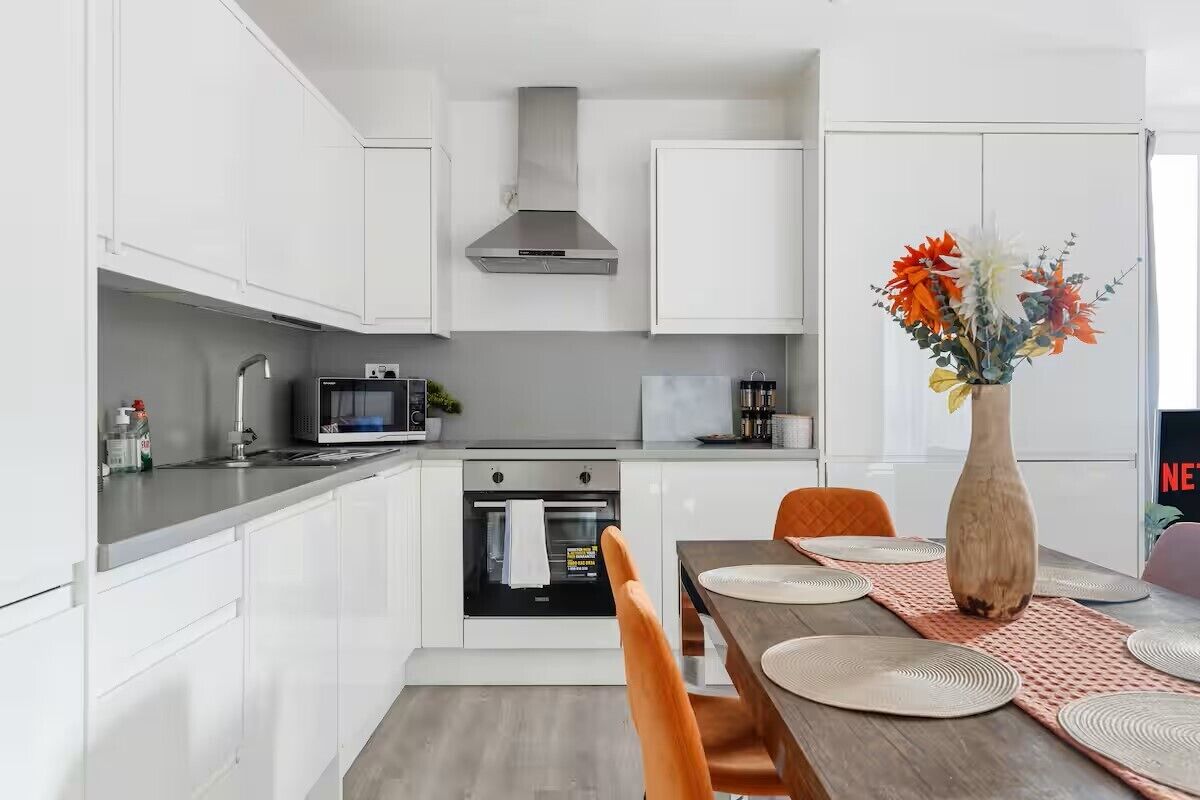 Une cuisine moderne avec des armoires blanches, une hotte de cuisinière en acier inoxydable, un four à micro-ondes et un four traditionnel.