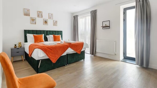 Une chambre à coucher avec un lit, une table de chevet, une chaise et une fenêtre avec des rideaux.