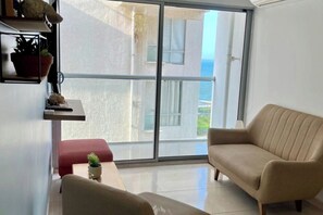 A living room with a sofa, a small table, and a potted plant. There is a sliding glass door leading to a balcony with a view of the sea. - Casa Arena Confort Torices (Cartagena de Indias)