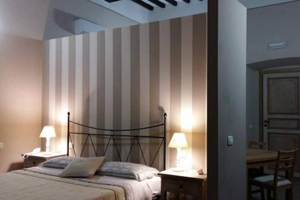 Une chambre à coucher comprenant un lit, des lampes de chevet, une table de chevet, une chaise, une table à manger et une porte.