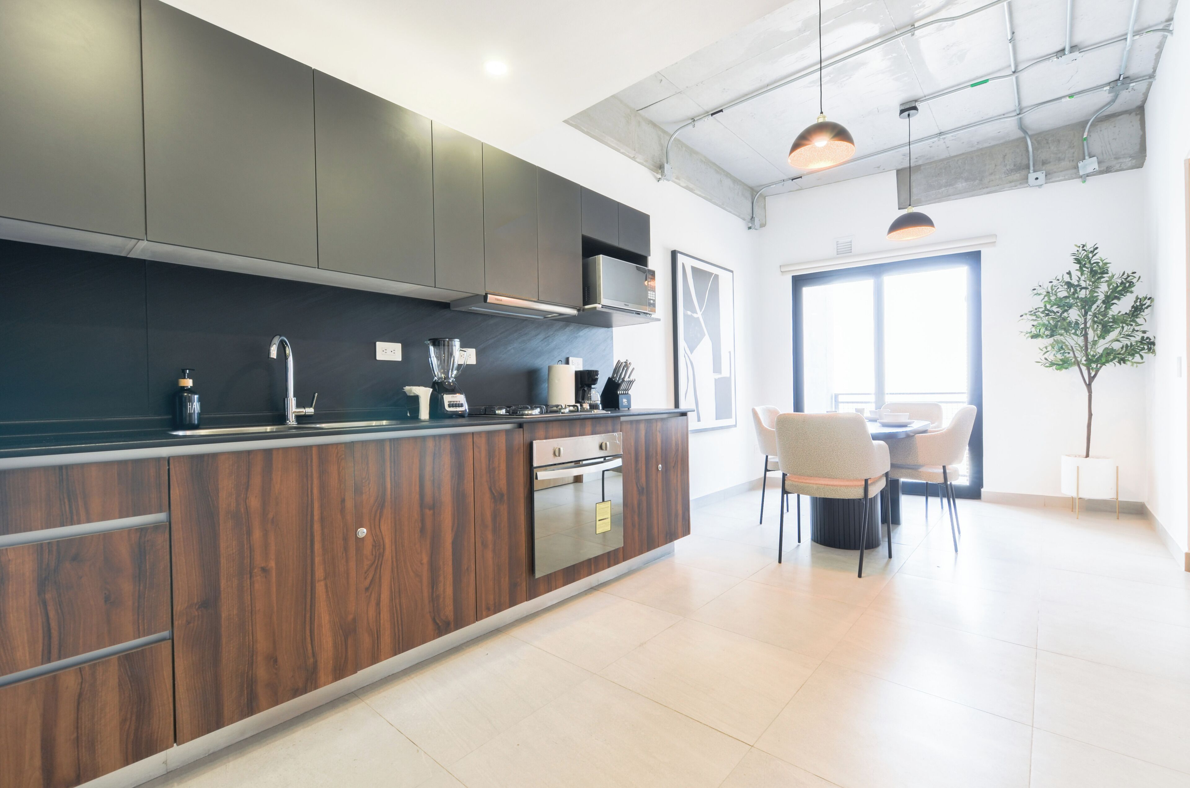 A modern kitchen with dark cabinetry, stainless steel appliances, and pendant lighting.