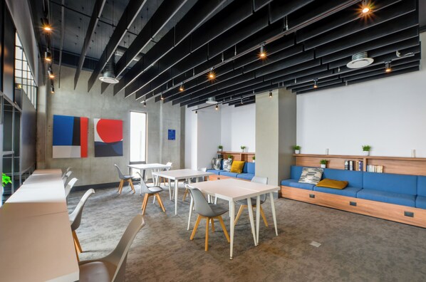 Un espace de bureau moderne avec une longue table, des chaises, un canapé bleu et un tableau blanc orné d’œuvres d’art abstraites.