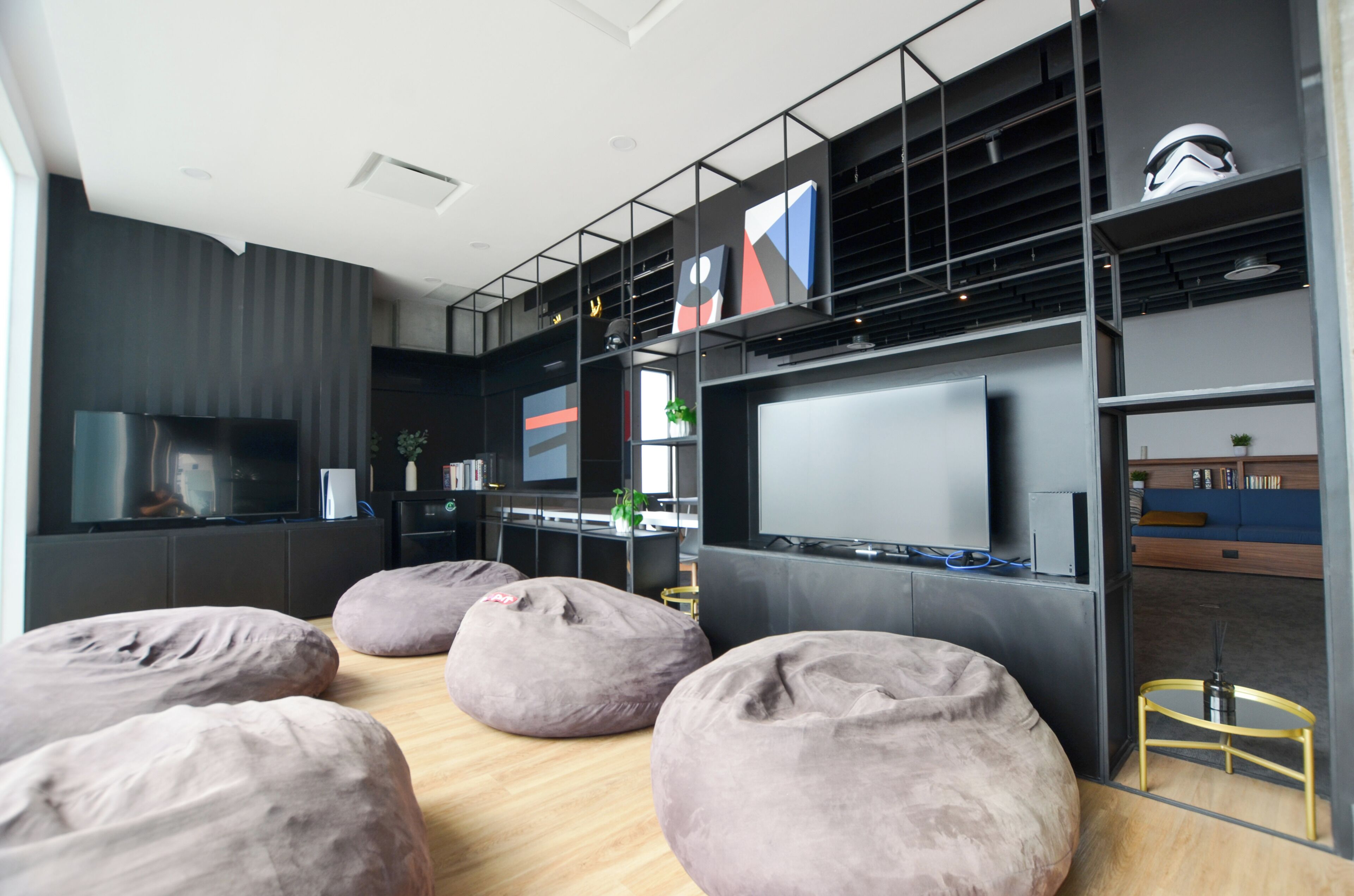 A modern living room with a large flat-screen TV, multiple bean bags, and a bookshelf.