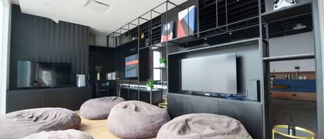 A modern living room with a large flat-screen TV, multiple bean bags, and a bookshelf.