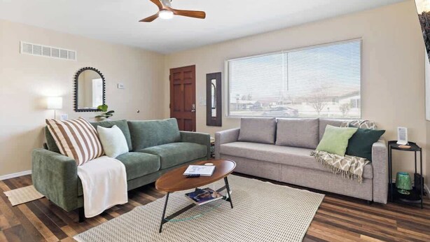 Ein Wohnzimmer mit zwei Sofas, einem Couchtisch, einem Deckenventilator, einem Fenster mit Jalousien und einer Tür.