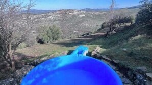 Un objet bleu se trouve dans un espace bordé de pierres, d’où l’on peut apercevoir des bâtiments et des collines au loin.
