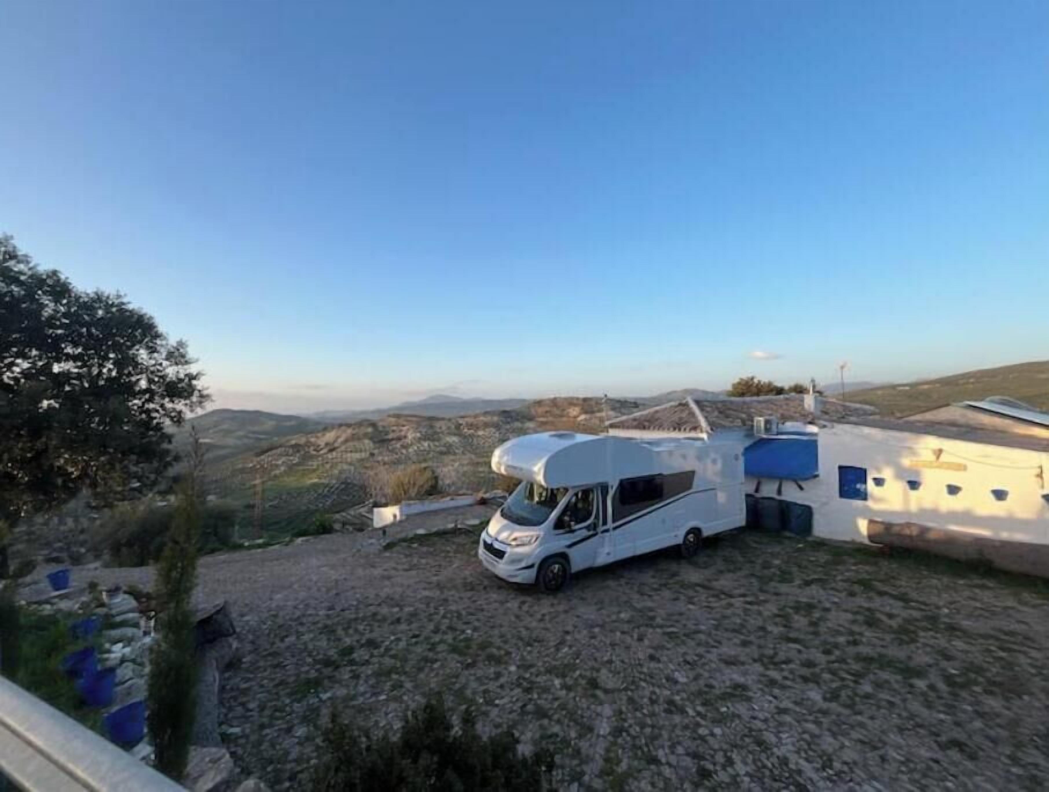 Una caravana blanca estacionada sobre grava, con un paisaje montañoso al fondo.