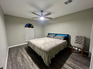A bedroom with a bed, a ceiling fan, a window with blinds, and a chair. - Two-in-one home in East Houston (Houston)