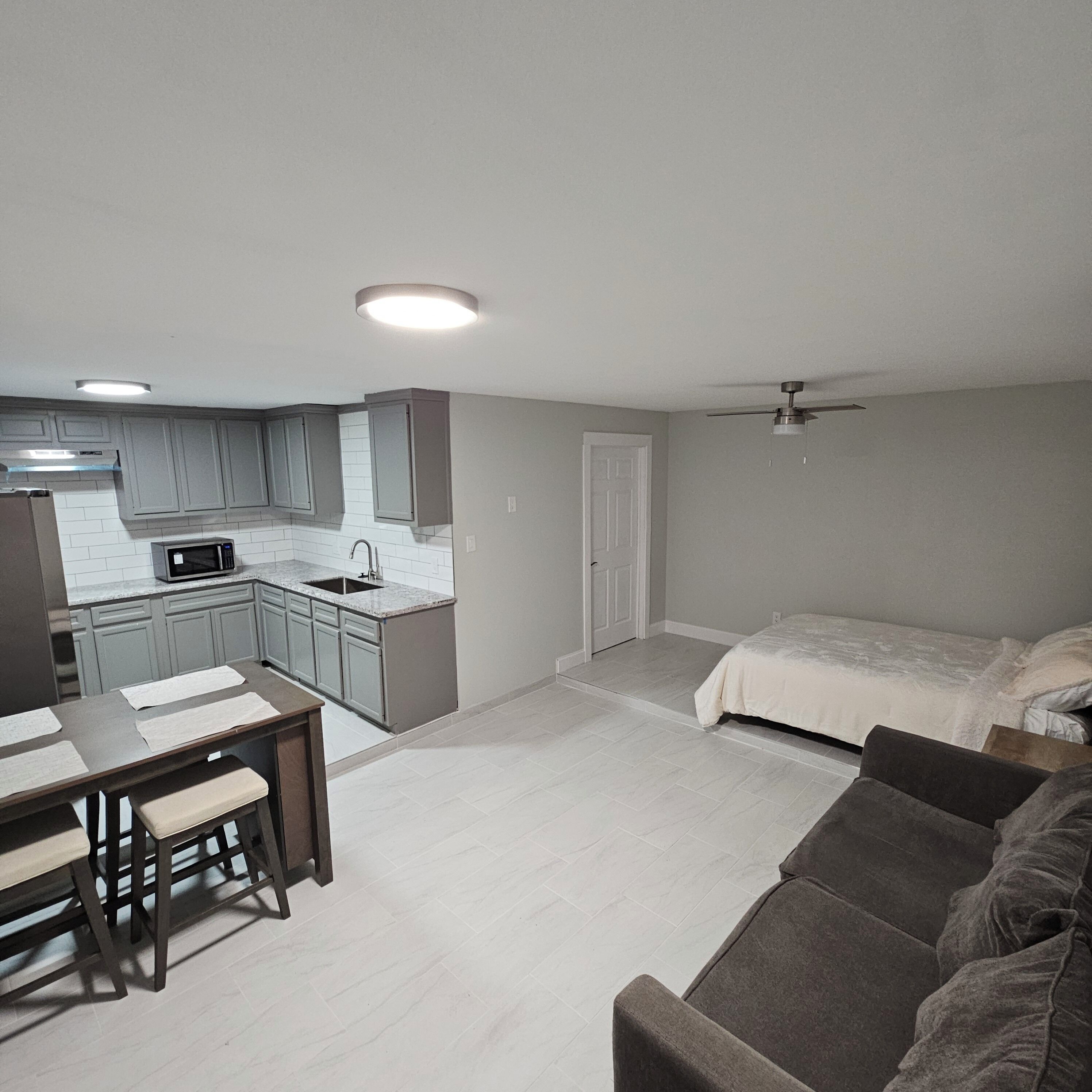 Un ambiente compatto con angolo cottura, zona pranzo, letto e ventilatore a soffitto.