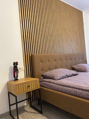 A bedroom with a bed, a nightstand, a wooden slat wall, and a small cabinet.