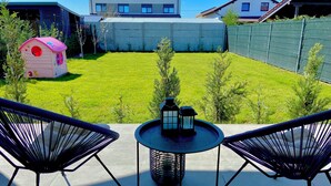 Een terras met twee stoelen en een tafel, een klein speelhuisje en een verzorgd gazon.