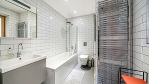 A modern bathroom with white subway tiles, a white sink, a bathtub, a toilet, and a shower. - Stylish Flat by Victoria Park (London)