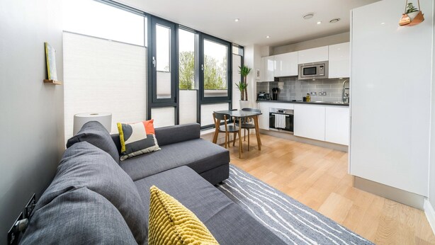 A modern living space with a sofa, dining table, and kitchen area. - Stylish Flat by Victoria Park (London)