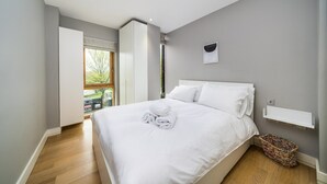 A modern bedroom with a large bed, a window, a bedside table, and a view of the outdoors. - Stylish Flat by Victoria Park (London)