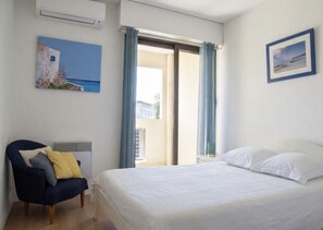 Ein Schlafzimmer mit einem Bett, einem Sessel, einem Fenster mit Vorhängen und einem Bild an der Wand.