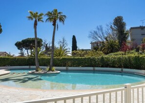Ein Swimmingpool mit Palmen, einer Hecke und einem Gebäude im Hintergrund.