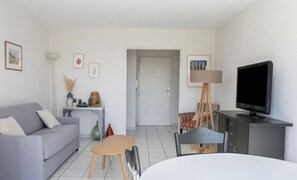 Ein modernes Wohnzimmer mit einem grauen Sofa, einem kleinen runden Tisch, einem Fernseher auf einer Kommode und einer Tür zu einem anderen Raum.