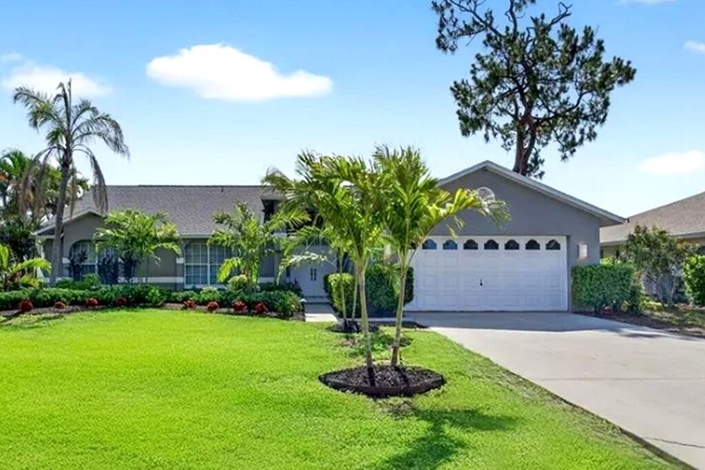 A residential house with a well-maintained lawn, a garage, and a large tree in the front yard.