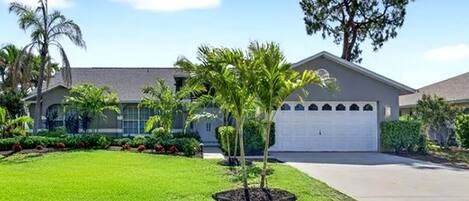 A residential house with a well-maintained lawn, a garage, and a large tree in the front yard.