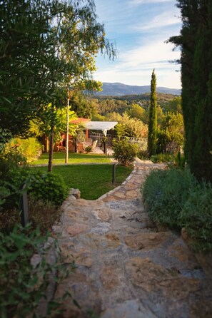 Ein steiniger Weg führt zu einem Haus mit Garten und Blick auf ferne Hügel.