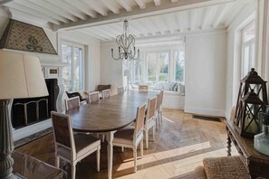 A dining room with a large wooden table, white chairs, a chandelier, and a fireplace. - Exceptional historic house with swimming pool (Yerres)