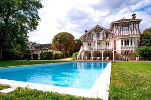 A large swimming pool with a two-story building featuring a balcony and a covered area with chairs. - Exceptional historic house with swimming pool (Yerres)