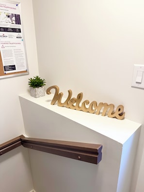 Un comptoir d’accueil avec une pancarte « Bienvenue », un tableau d’affichage et une plante en pot.