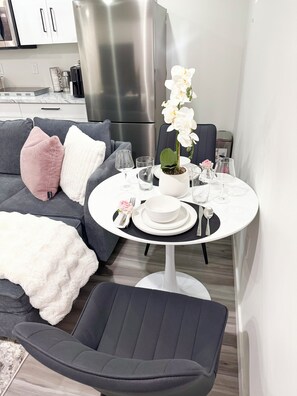 Un salon moderne avec un canapé gris, une table blanche mise avec de la vaisselle et une orchidée en pot.
