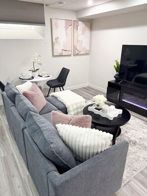 A modern living room with a grey sectional sofa, a black armchair, a round coffee table, a flat-screen TV, and a fireplace.