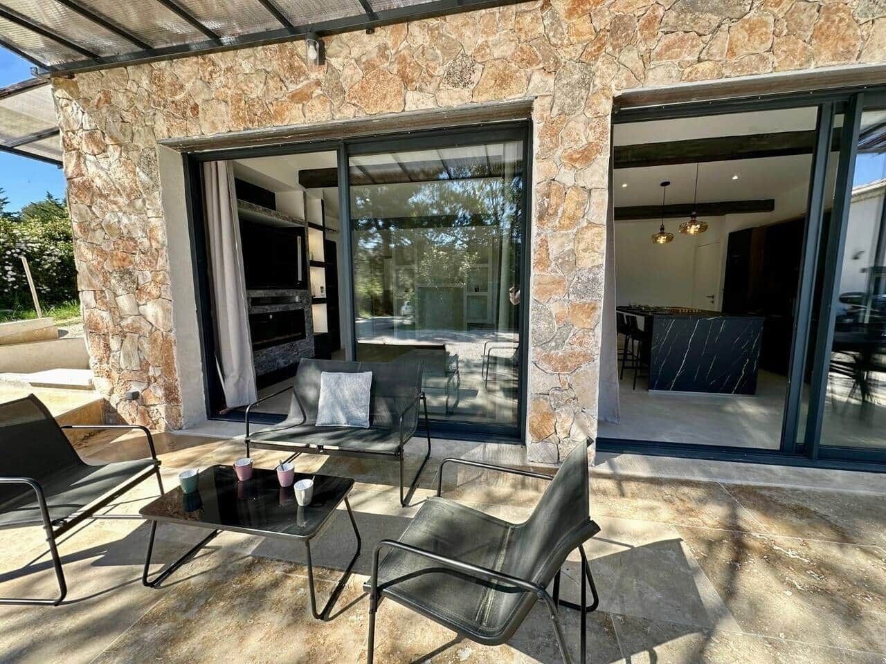 Une terrasse avec des sièges extérieurs, un mur en pierre et une porte vitrée donnant sur un espace intérieur.