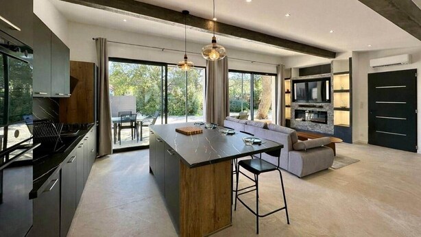 A modern kitchen with a central island, built-in appliances, and a large window.