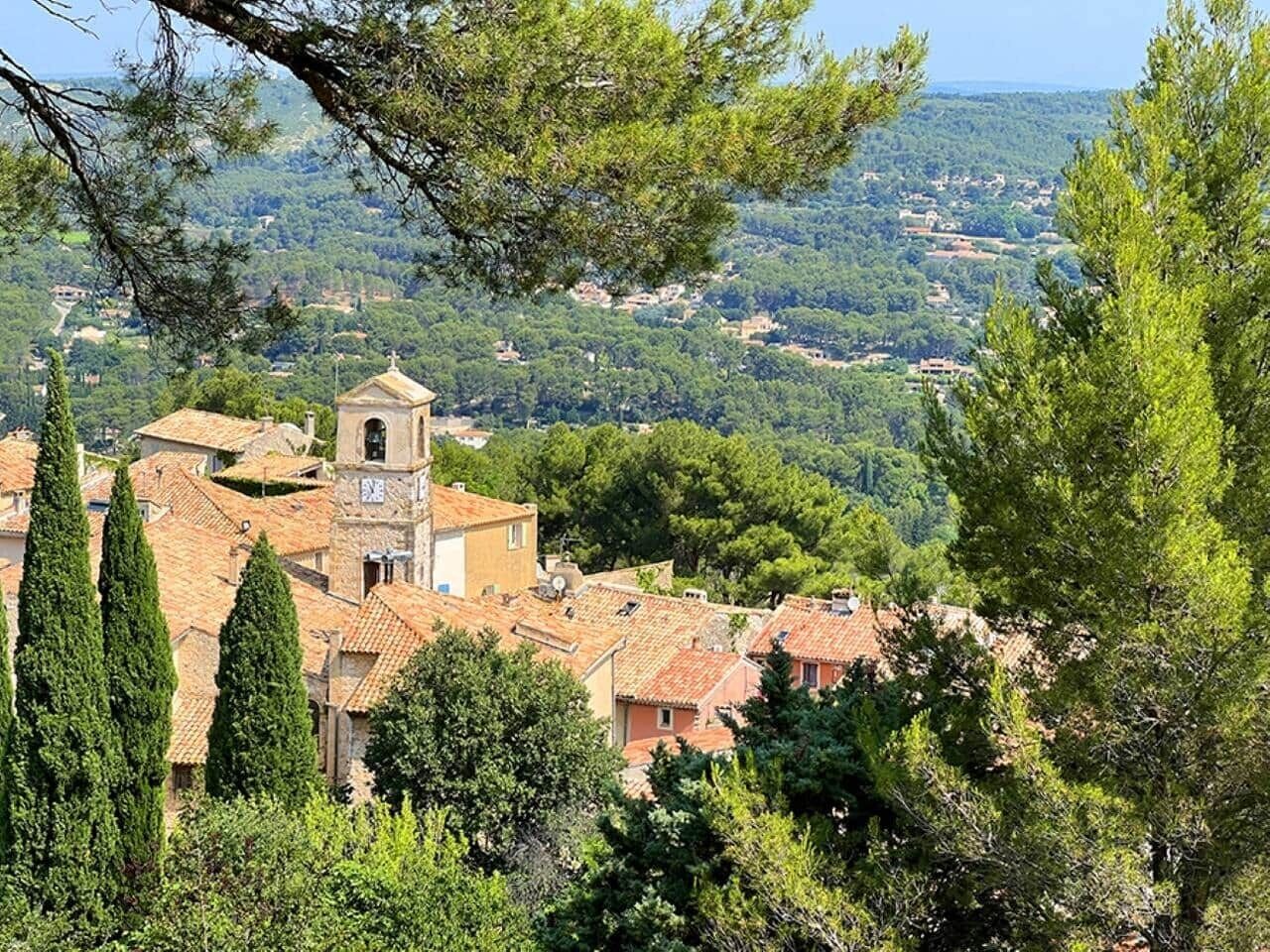 Un village pittoresque, avec une église imposante dotée d’un clocher, entouré de verdure et de bâtiments traditionnels.