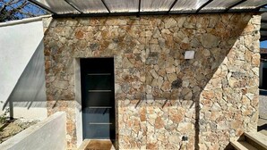 A stone wall entrance with a door, a welcome mat, and a metal roof structure.
