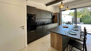 A modern kitchen with dark cabinetry, a marble countertop, and a dining area with a table and chairs.