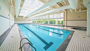 Une piscine intérieure dotée d’un plafond en verre transparent, d’un sol carrelé et d’une horloge visible au mur.