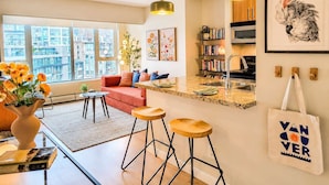 Un salon moderne avec un canapé, une table basse et des tabourets de bar. On y trouve également un coin cuisine avec un évier et une bibliothèque.