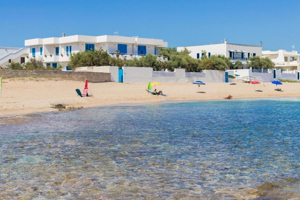 Een hotel aan het strand met witte gebouwen, helderblauw water en een zandstrand.